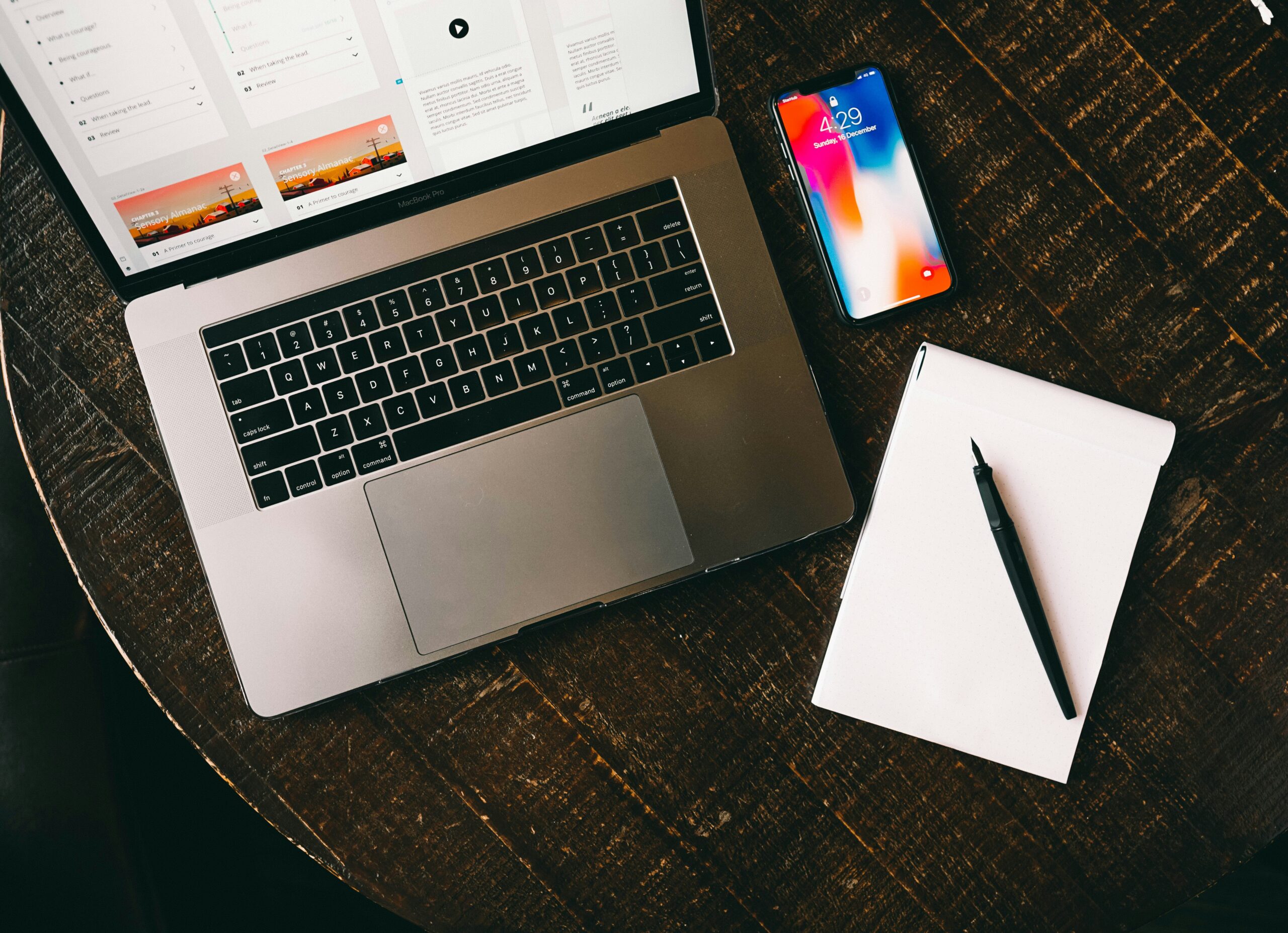 Open laptop on a wooden desk next to an empty notebook.
