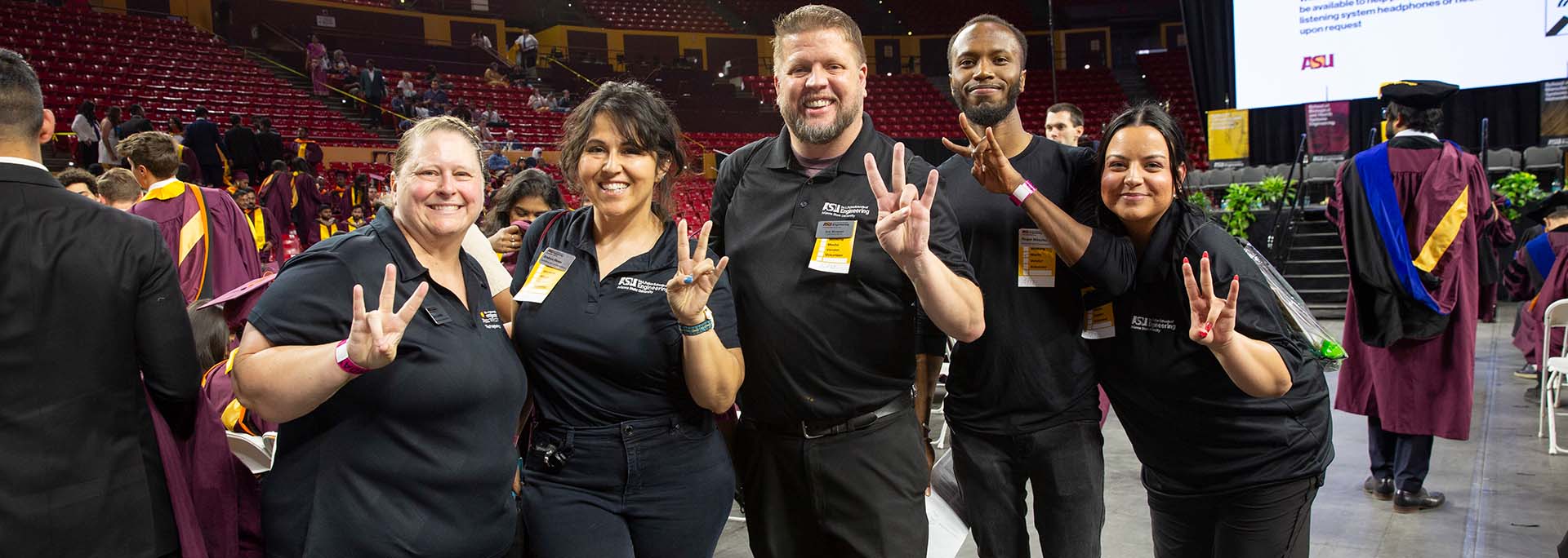 Five marketing and communications team members stand together, all in black, at a Spring 2025 convocation ceremony in Desert Financial Arena at Arizona State University.